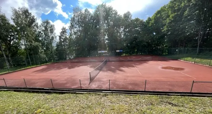 Brun tennisbana med skog i bakgrunden