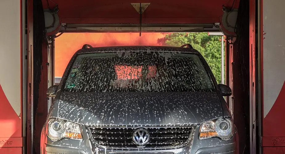 En grå bil i en biltvätthall med schampo på hela framrutan