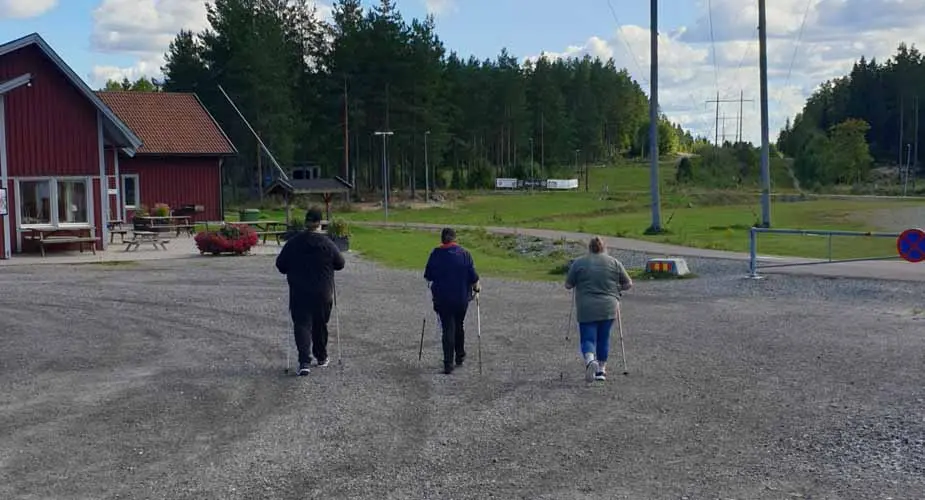 Tre personer går stavgång på ett grusat motionsspår