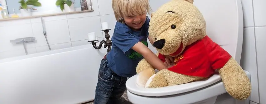En liten pojke som försöker trycka ner en stor nalle i toaletten