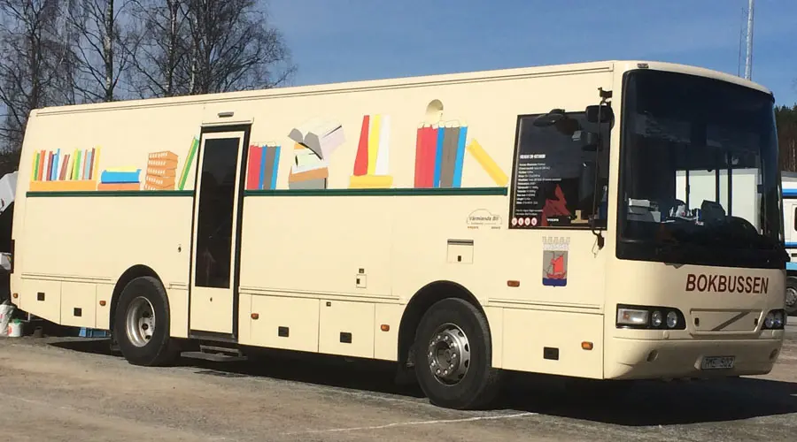 En beige buss med böcker målade på utsidan av bussen och texten bokbuss.