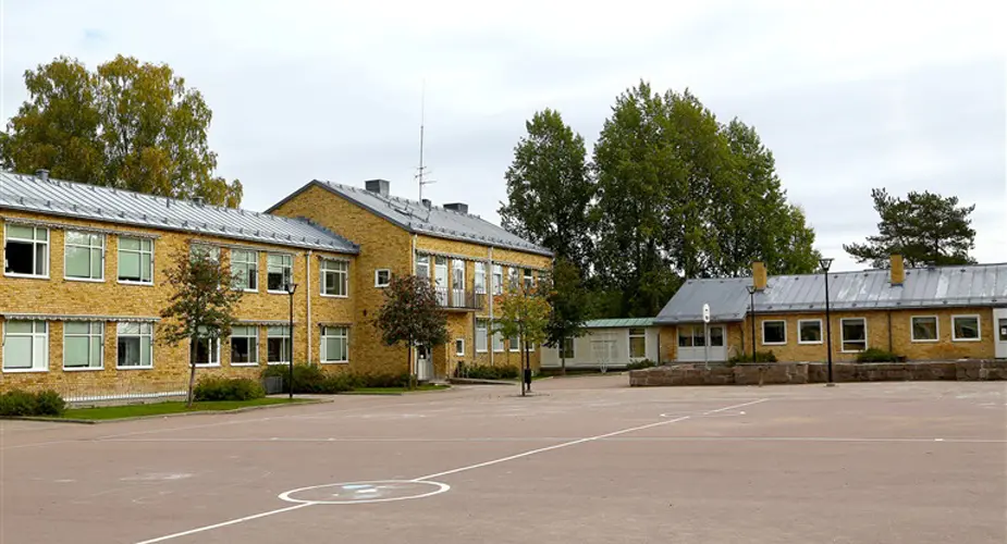 Strandvägsskolan. En stor skolgård med två gula tegelbyggnader i bakgrunden