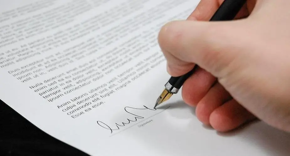 Närbild på hand som skriver namnteckning på ett långt dokument