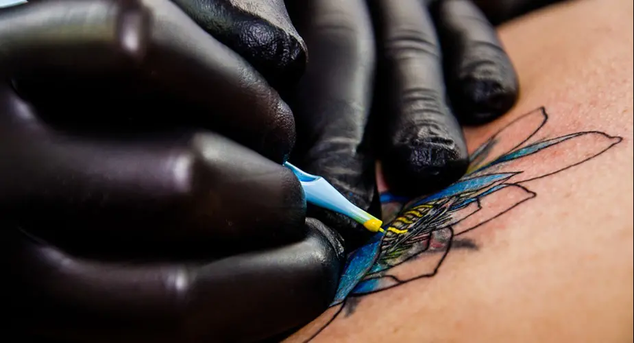 En tatuerare med svarta handskar tatuerar en blå blomma