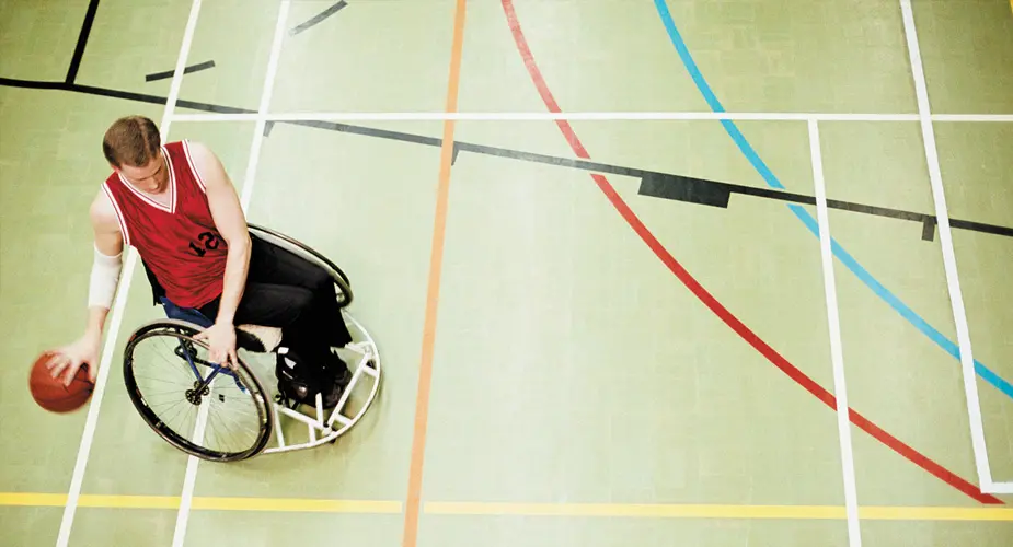 Person i rullstol spelar basket i en idrottshall