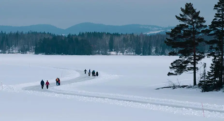 Snötäckt is på håll med skog runtom. Flera sällskap går på ett plogat is-spår.
