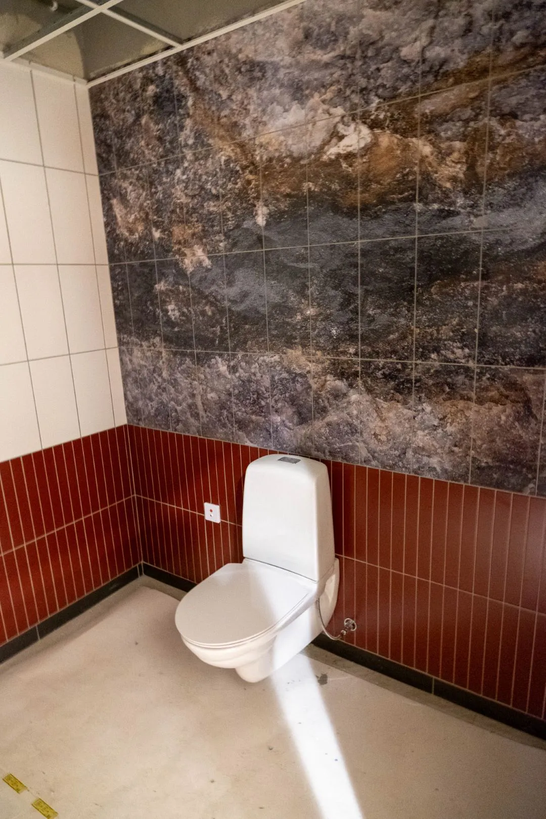 Toalett med rött och vitt kakel. Bakom toaletten är ett väggmotiv med mineraler