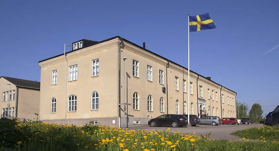 Bergskolans byggnad, en chremé-färgad fasad med fönster med vita ramar. En flaggstång med svensk flagga.