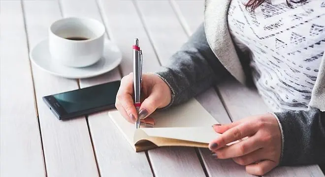 Kvinna skriver anteckningar med kaffekopp och mobil på bordet
