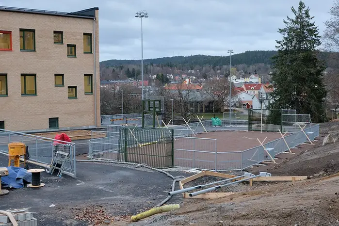 En sportplan med staket, fotbollsmål och basketkorgar under uppbyggnad.