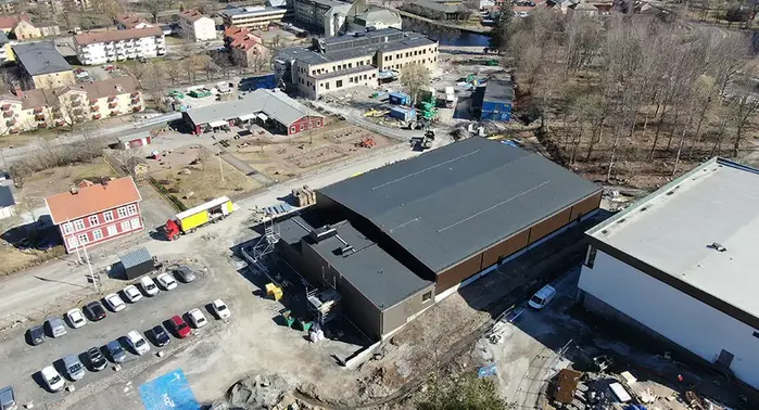 Drönarbild över idrottshallens mörka tak med byggarbetsplats intill